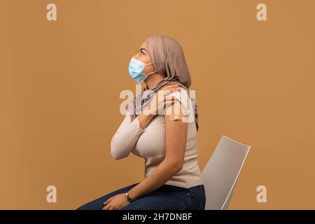 Muslimische Frau in Gesichtsmaske mit Haftverband auf der Schulter nach covid Impfstoff Schuss, Blick auf den Kopierraum Stockfoto