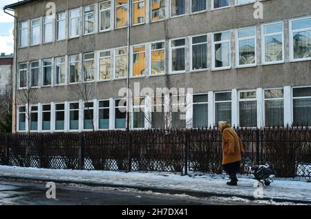 Eine alte Frau im Rentenalter mit einer Tasche auf Rädern läuft allein die Straße in der Nähe des Krankenhauses entlang, eine einsame Rentnerin, kovid19, die im frischen Wind geht Stockfoto