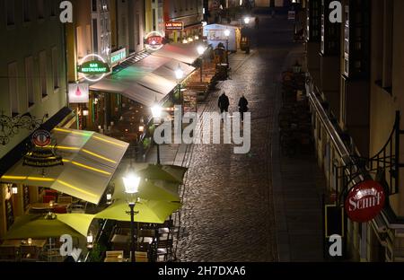 Dresden, Deutschland. 22nd. November 2021. Passanten laufen am Abend durch die Münzgasse an Restaurants und Bars vorbei. Angesichts der rasant steigenden Corona-Zahlen gelten ab diesem Montag unter anderem in Sachsen und Schleswig-Holstein strengere Regeln zur Bekämpfung der Pandemie. Sachsen, das besonders betroffen ist, schränkt große Teile des öffentlichen Lebens ein. Quelle: Robert Michael/dpa-Zentralbild/dpa/Alamy Live News Stockfoto