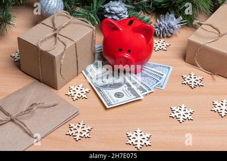 Ein Sparschwein, das auf Bargelden auf einem Tisch mit Geschenkschachteln, Schneeflocken und Tannenzweigen steht. Das Konzept von Erfolg und Wohlstand im Neuen Stockfoto