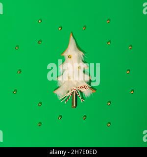 Wealth Christmas Komposition. Grüner Hintergrund. Hölzerner und weißer Weihnachtsbaum. Kleine goldene Kugeln als Dekoration. Asymmetrische Anordnung von golden Stockfoto
