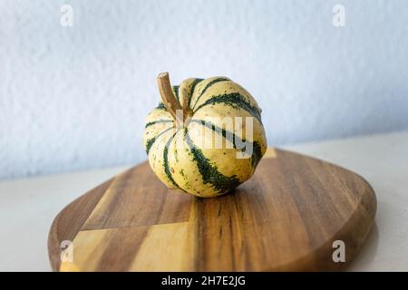 Ein cremefarbener und grüner Mini-Kürbis, der auf einem hölzernen Schneidebrett steht Stockfoto