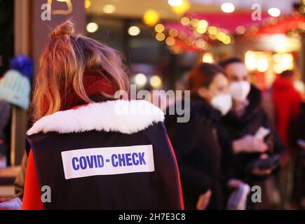 Köln, Deutschland. 22nd. November 2021. Eine von den Ausstellern eingesetzte Inspektorin, die auf ihrem Rücken ein Schild mit der Aufschrift „Covid Check“ trägt, geht durch den Weihnachtsmarkt auf dem Roncalliplatz in der Nähe des Doms, um die Regeln von 2G zu überprüfen. Die Weihnachtsmärkte in Köln sind nach den Regeln von 2G für Besucher geöffnet. Quelle: Oliver Berg/dpa/Alamy Live News Stockfoto