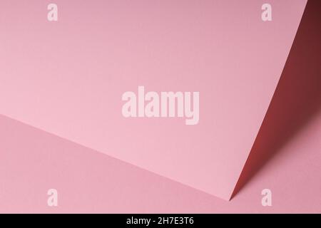 Unbeschriftete, pastellrosa Papierkarte mit Schatten. Abstrakter geometrischer monochromer rosafarbener Hintergrund mit Platz für Text. Diagonale Vorderansicht Stockfoto