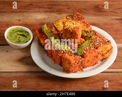 Masala Dhokla aus Reis oder Urad dal ist ein beliebtes Frühstück oder Snacks Rezept aus Gujarat, Indien, serviert mit Green Chutney und gebratenen Chili. Se Stockfoto