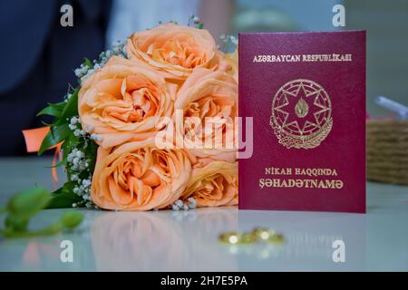 Aserbaidschan Baku 7.07.2020 . Heiratsurkunde der Republik Aserbaidschan.Verlobungsringe aus Gelbgold vor dem Hintergrund eines Straußes aus fl Stockfoto