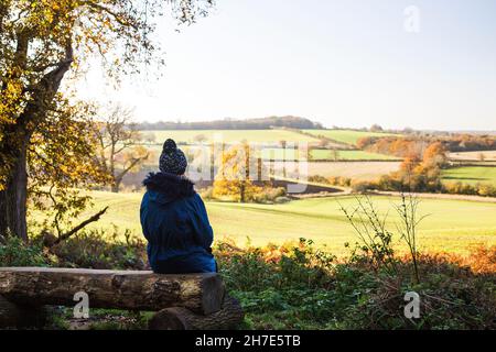 Eine junge Frau mit Outdoor-Ausrüstung sitzt an einem hellen, sonnigen Herbsttag auf einer Holzbank mit Blick auf die Landschaft von Oxfordshire. Stockfoto