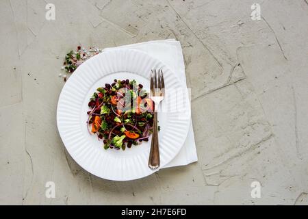 Veganer energiesteigerender Salat mit Bohnen, Brokkoli, Tomaten, roten Zwiebeln, Sproots und Kürbiskernen Stockfoto