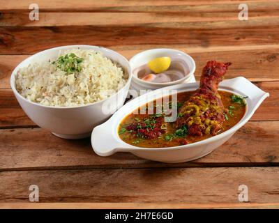 Traditionelle indische Küche, Chicken-Kerrisch und gekochter Reis auf einer weißen Keramikschüssel auf rustikalem Holzhintergrund mit Zitrone und Zwiebel Stockfoto