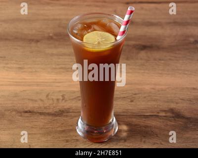 Traditioneller Eistee in einem Glas mit Zitrone und Papierhalmen auf einem rustikalen Holzhintergrund. Stockfoto