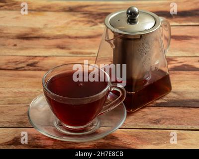 Frisch gebrühter Cranberry-Apfel-Tee in einer Glasschale mit Teekocher auf rustikalem Holzhintergrund, selektiver Fokus Stockfoto