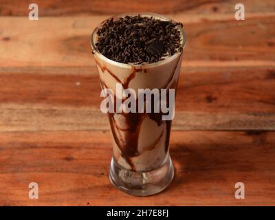 Kalter Kaffee in einem hohen Glas mit Schokoladenwürmchen auf einem alten rustikalen Holztisch. Stockfoto