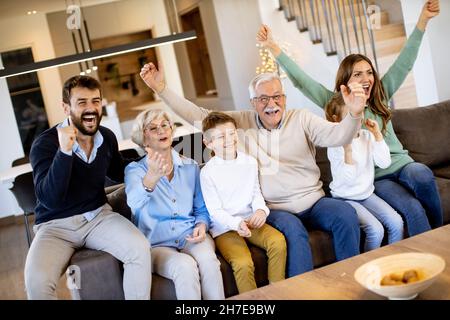 Eine Familie mit mehreren Generationen, die Fußball im Fernsehen sieht und ein Tor feiert, sitzt auf der Couch im Wohnzimmer Stockfoto