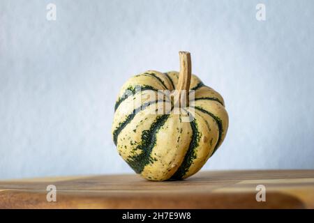 Ein cremefarbener und grüner Mini-Kürbis, der auf einem hölzernen Schneidebrett aufsteht Stockfoto