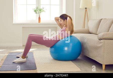 Glücklich fit junge Frau dabei Sit-ups auf Gymnastikball während Fitness-Training zu Hause Stockfoto