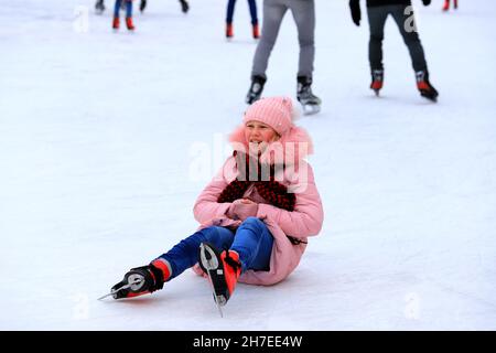 Das Mädchen geht Eislaufen und fällt auf die Kindereisbahn. Sportverletzung, Beinschmerzen, Bruch bei sportlichen Aktivitäten, Winterpause Weihnachten. Dnipro Stockfoto