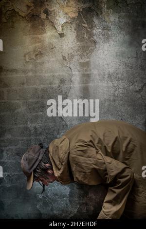 Junkie Mann mit Mütze grün Anorak und blaue Jogginghose in der Nähe Stein alten Wand Stockfoto