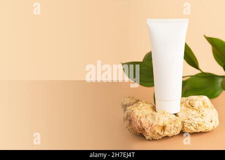 Blanke Kosmetikröhre, die auf den natürlichen dekorativen Steinen auf dem pastellfarbenen isometrischen Hintergrund bleibt. Stockfoto