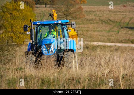 Großer blauer Traktor aus New Holland, ausgestattet mit Heckenschnitt, der durch das Land fährt, Wiltshire UK Stockfoto