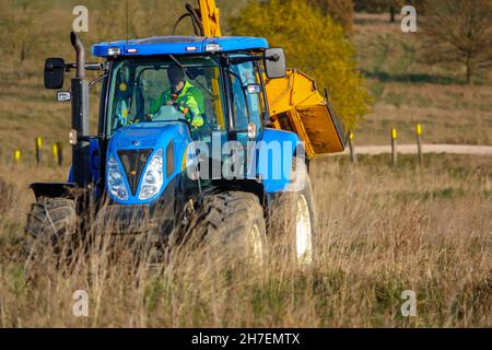 Großer blauer Traktor aus New Holland, ausgestattet mit Heckenschnitt, der durch das Land fährt, Wiltshire UK Stockfoto