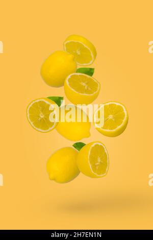 Saftig reife ganze und geschnittene Zitronen fliegen auf gelbem Hintergrund. Kreatives Food-Konzept. Tropische Bio-Früchte, Zitrusfrüchte, Vitamin C. Minimaler Sommerfruit Stockfoto