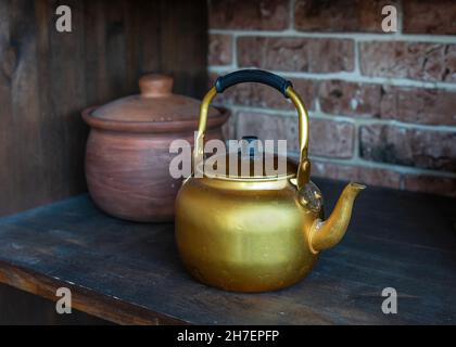 Uralter Goldkessel auf altem Holzregal. Klassische Teekannen zum Trinken von Tee oder Kaffee. Tontopf im Hintergrund. Stockfoto