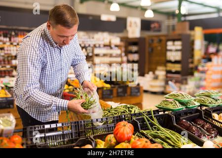 Mann, der grüne Bohnen im Supermarkt wählt Stockfoto