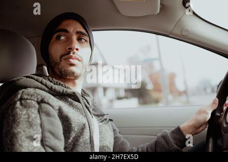 30-etwas gemischter junger Tausendjähriger, der in einem älteren Auto fährt, um Besorgungen zu machen. Ernsthafter Ausdruck beim Navigieren Stockfoto