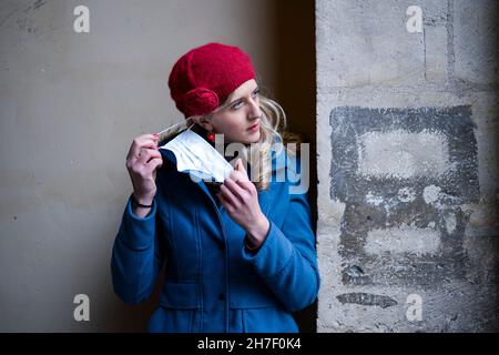 Eine junge blonde Frau mit blauen Augen zieht ihre Anti-Covid 19 Maske während der Sperre in einer Straße in Paris aus Stockfoto