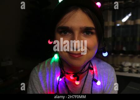 Weihnachts Nahaufnahme Porträt. Flippige junge Frau, die Weihnachten feiert. Junge Person, die Spaß in den Winterferien mit bunten Lichtern hat. Frau Stockfoto