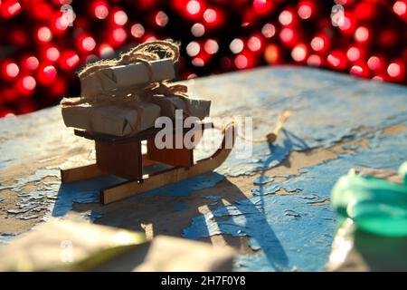 Weihnachtsdekoration. Eingewickelte Vintage Geschenkschachteln liegen Holzspielzeug Schlitten auf blauem alten Holzhintergrund. Geschenk-Box in Bastelpapier. Urlaub Stockfoto