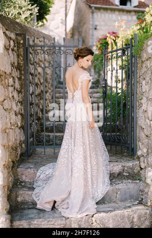 Braut in einem Kleid steht auf der Steintreppe vor dem geschmiedeten Tor des Hauses Stockfoto