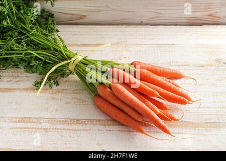 Bund von Bio-Karotten mit frischem Grün aus dem Markt auf einem hellen rustikalen Holztisch, Kopierraum, ausgewählter Fokus, enge Schärfentiefe Stockfoto
