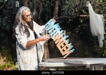 Frau mit grauem Haar, die im Garten einige Buchstaben aus Polystyrol gemalt hat Stockfoto