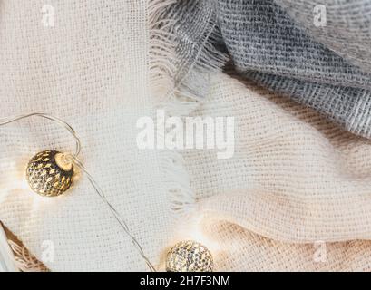 Frauen Mode Winterkleidung und Accessoires. Damen-Look mit gestricktem weißen und rosa Schal, Girlanden auf beigem pastellfarbenem Hintergrund. Stockfoto