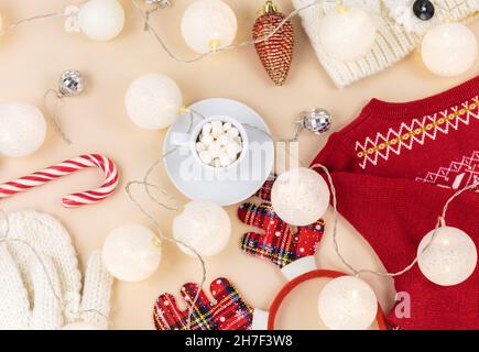 Tasse Kaffee, Geschenkbox und Strickpullover, LED-Leuchten auf beigem Hintergrund. Hygge-Stil, Winterkonzept. Gemütlicher Schreibtisch. Neujahr und Weihnachten Stockfoto