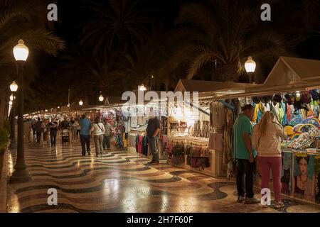 Paare, Männer und Frauen gehen spazieren und schauen sich Gegenstände an den Ständen an, die Kunsthandwerk auf dem Nachtmarkt auf der Esplanada de España in Alicante verkaufen Stockfoto