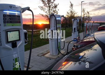 Elektrofahrzeuge laden bei Sonnenuntergang auf dem Gridserve Electric Highway Schnellladegeräte in Rugby, England Stockfoto