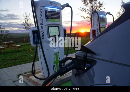 Elektrofahrzeug angeschlossen und bei Sonnenuntergang an einem Gridserve Electric Highway-Hochleistungsladegerät in Rugby, England, aufgeladen Stockfoto