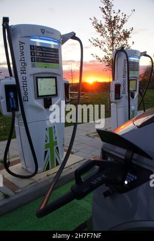 Elektrofahrzeug angeschlossen und bei Sonnenuntergang an einem Gridserve Electric Highway-Hochleistungsladegerät in Rugby, England, aufgeladen Stockfoto