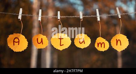 Das Wort Herbst steht auf den Herbstblättern, die am Seil hängen. Herbstkonzept. Stockfoto