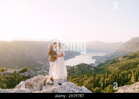 Braut und Bräutigam stehen auf einem felsigen Berg mit Blick auf die Bucht Stockfoto