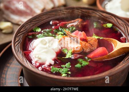 Frisch gekochtes Borscht: Traditionelles Gericht der russischen und ukrainischen Küche in Steingutgerichten mit Speck, Brot, Sauerrahm und Knoblauch, Nahaufnahme. Stockfoto