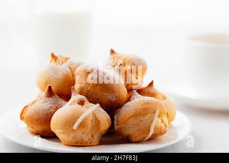 Morgenkaffee mit Kuchen. Profiterolen, Kaffee, Creme auf einem weißen Holztisch Stockfoto