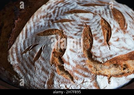 Hausgemachtes rundes dunkles Brot mit Mehlkruste und bemalten Stacheletts aus nächster Nähe Stockfoto