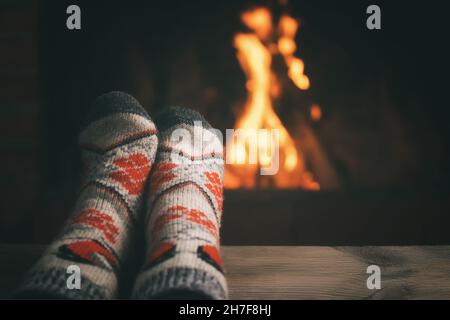 Mädchen, das sich an einem Winterabend in einem Landhaus an einem brennenden Kamin ausruhte und ihre Füße wärmte. Stockfoto