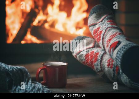 Mädchen, das sich an einem Winterabend in einem Landhaus an einem brennenden Kamin ausruhte und ihre Füße wärmte. Stockfoto