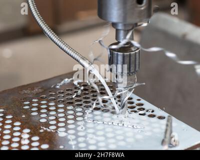 Säulenbohrmaschine, die in einer Industriewerkstatt millfache Löcher in einer Stahlplatte macht. Geringe Schärfentiefe und Bewegungsunschärfe. Stockfoto