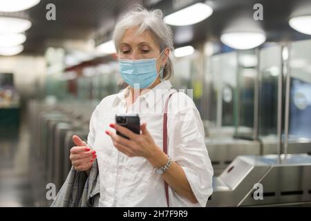 Ältere Frau in Maske, die ihr Telefon am Eingang zur U-Bahn-Station benutzte Stockfoto