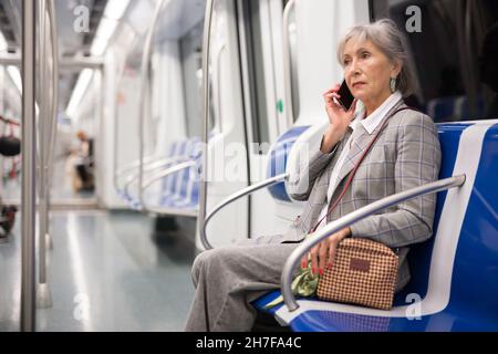 Ältere Frau, die im U-Bahn-Zug telefoniert Stockfoto